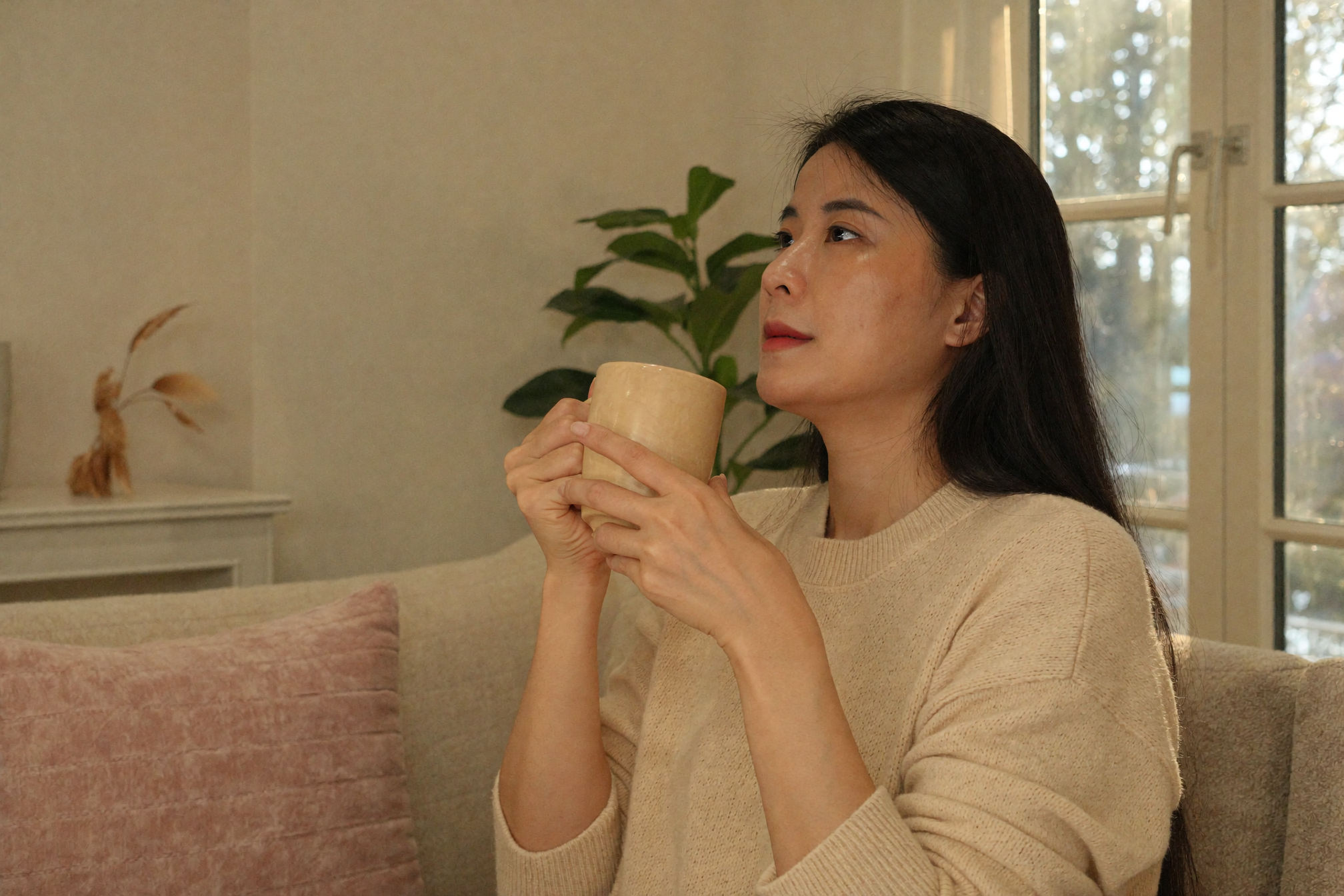 woman vietnamese calm storytelling sofa cream sweater warm mug afternoon light — Phụ nữ ngồi sofa kể chuyện bình thản cầm cốc nước ấm