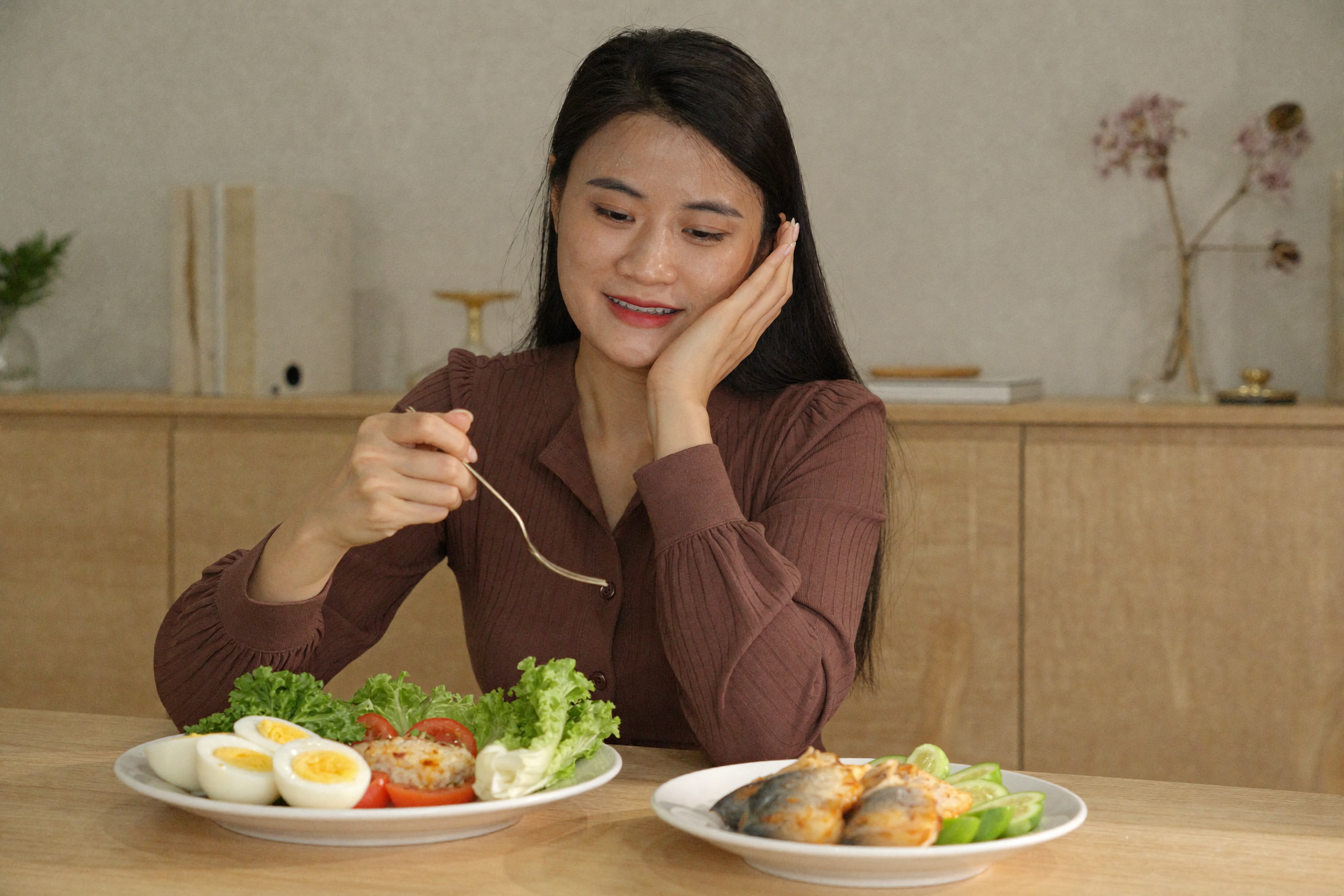 woman vietnamese healthy breakfast plate eggs vegetables fish wood dining table — Phụ nữ ngồi bàn ăn gỗ với đĩa trứng rau cá cười nhẹ